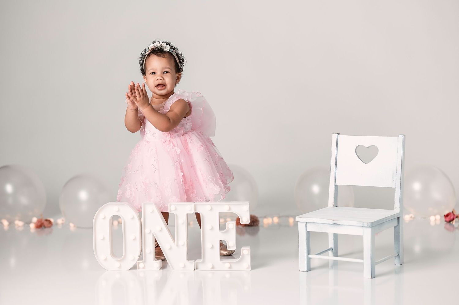 Baby girl in pink tutu dress standing near marquee ONE sign in first birthday photo session.
