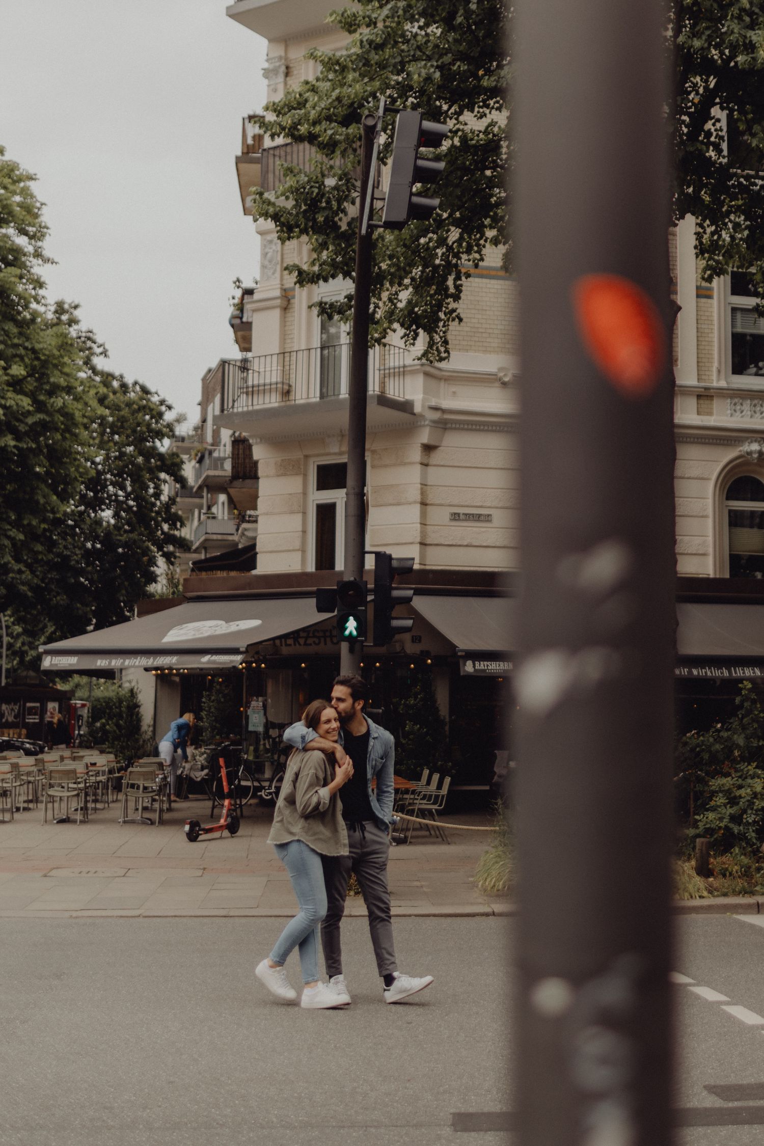 Couple walking together on urban street with historic building and cafe in background.