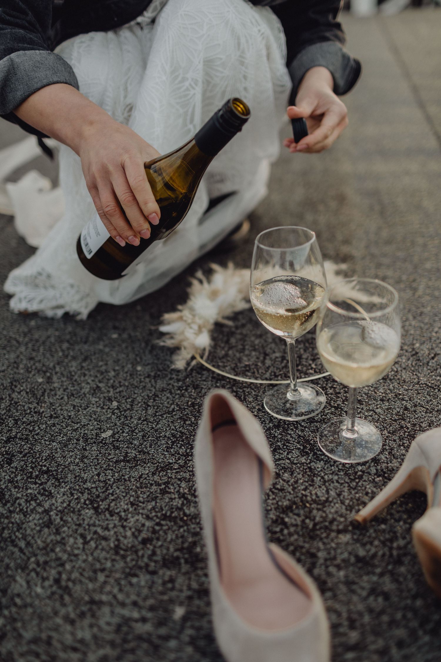 Wine glasses and high heels on carpet with someone pouring white wine.