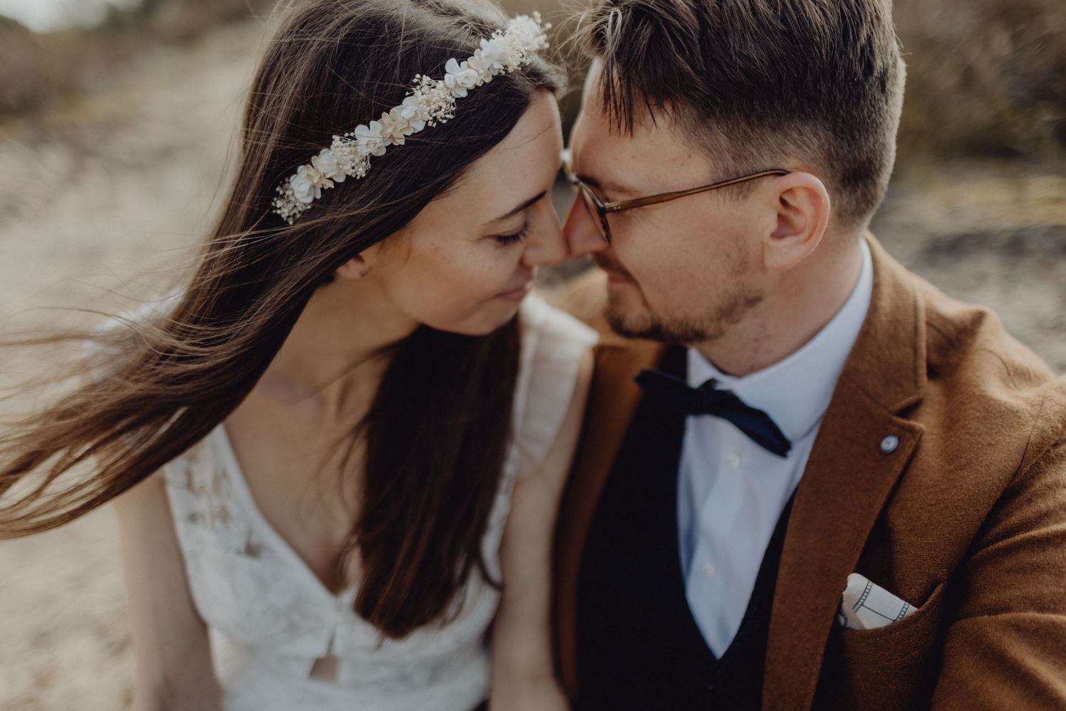 Romantic close-up of wedding couple touching foreheads against natural backdrop.