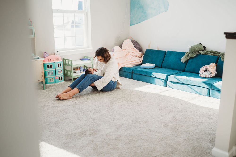 Fun playtime moments on grey carpet in bright, modern room with teal furniture.