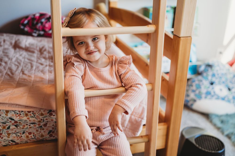 Child in pink sweater sitting at wooden table with toys.