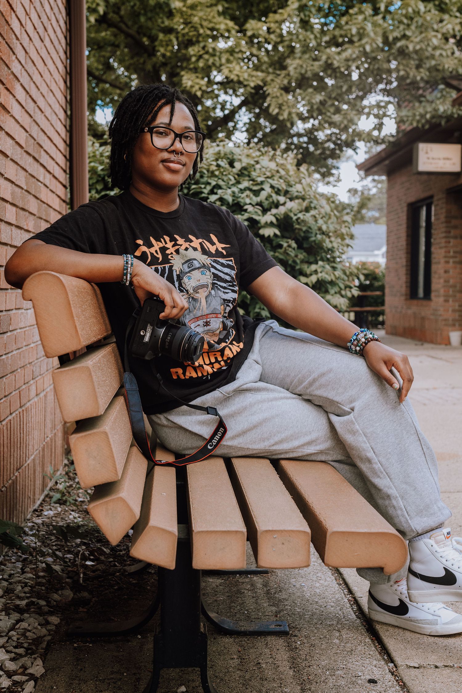 Casual photographer sits on wooden bench wearing graphic tee and light jeans.