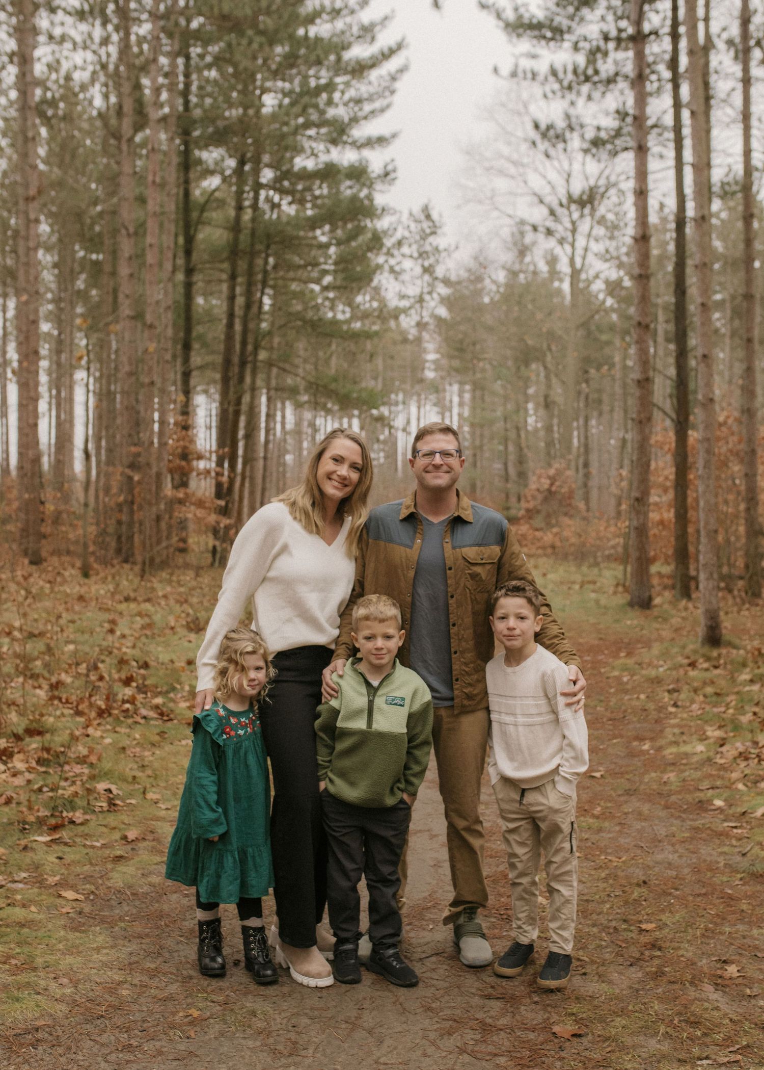 A family of four poses together in an autumn forest setting wearing casual clothing.