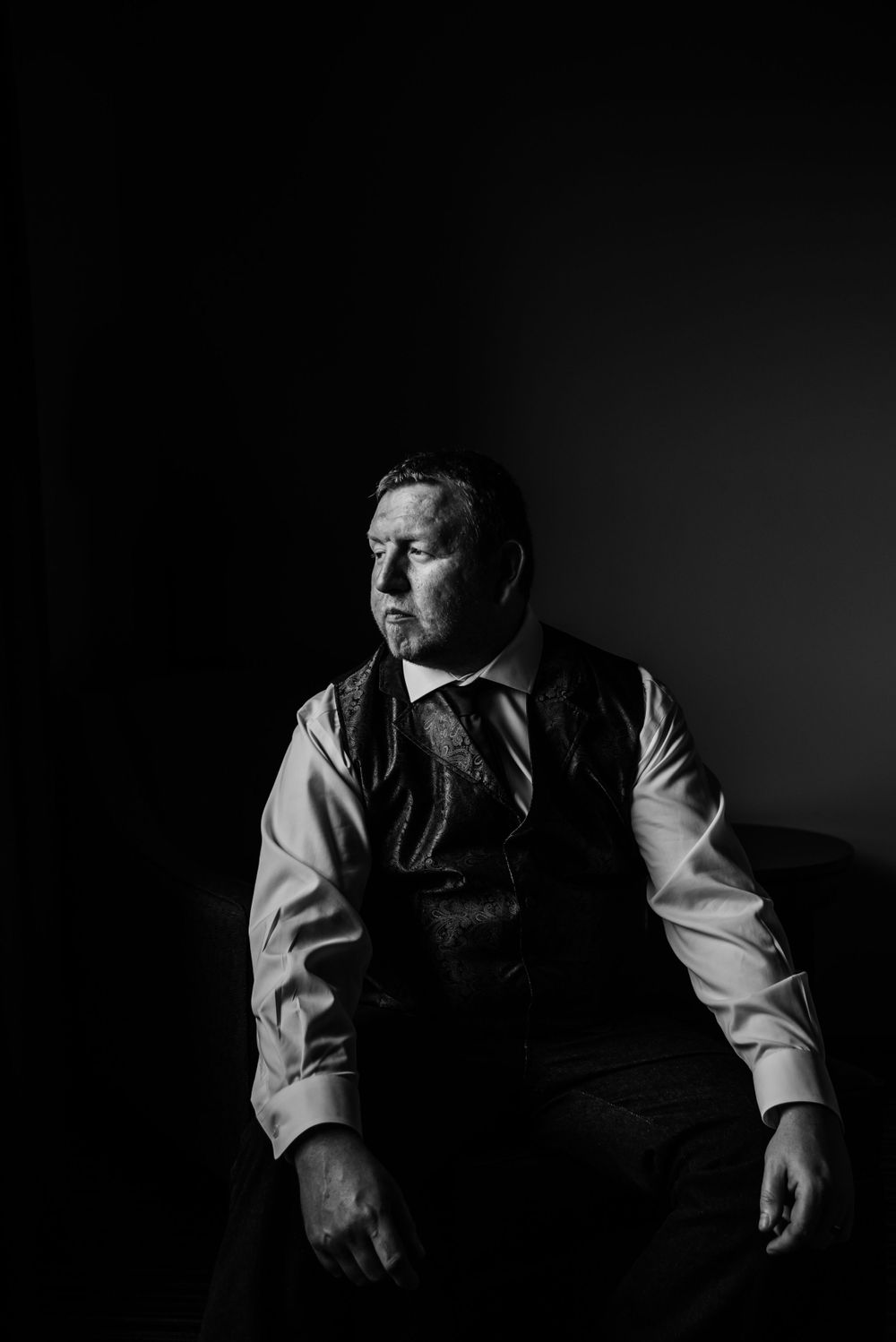 Dramatic black and white portrait of a groom in vest and dress shirt looking to the side.