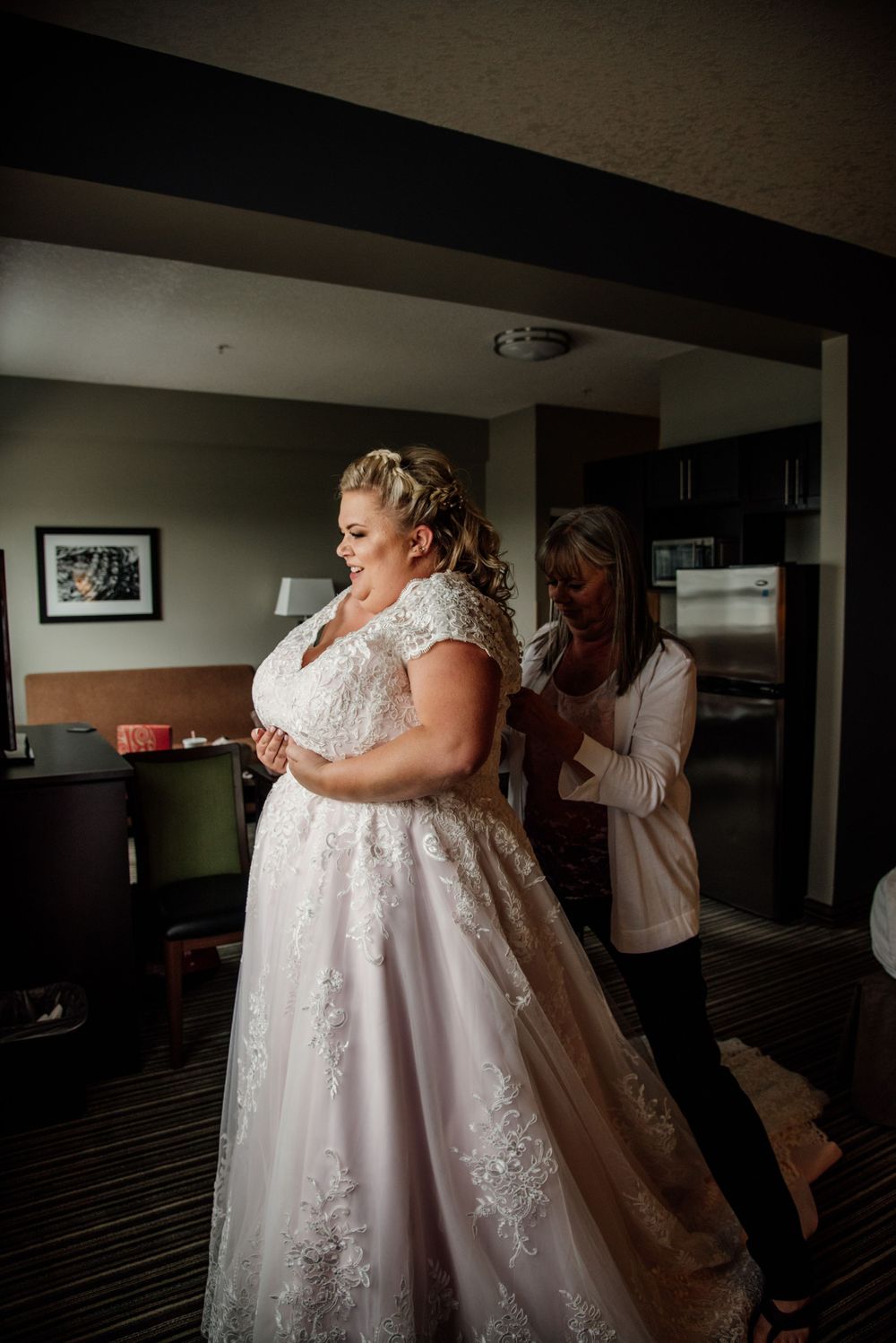 Person in lace wedding dress getting final adjustments in preparation room.
