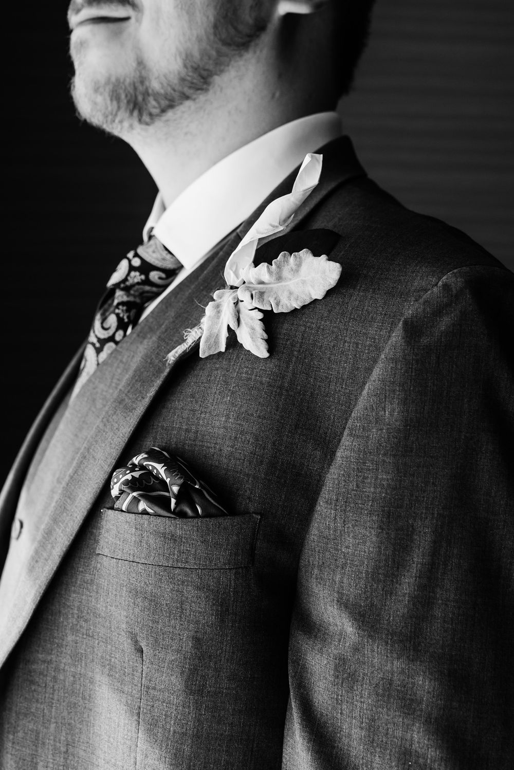 Close-up of grey suit jacket with floral boutonniere and patterned pocket square.