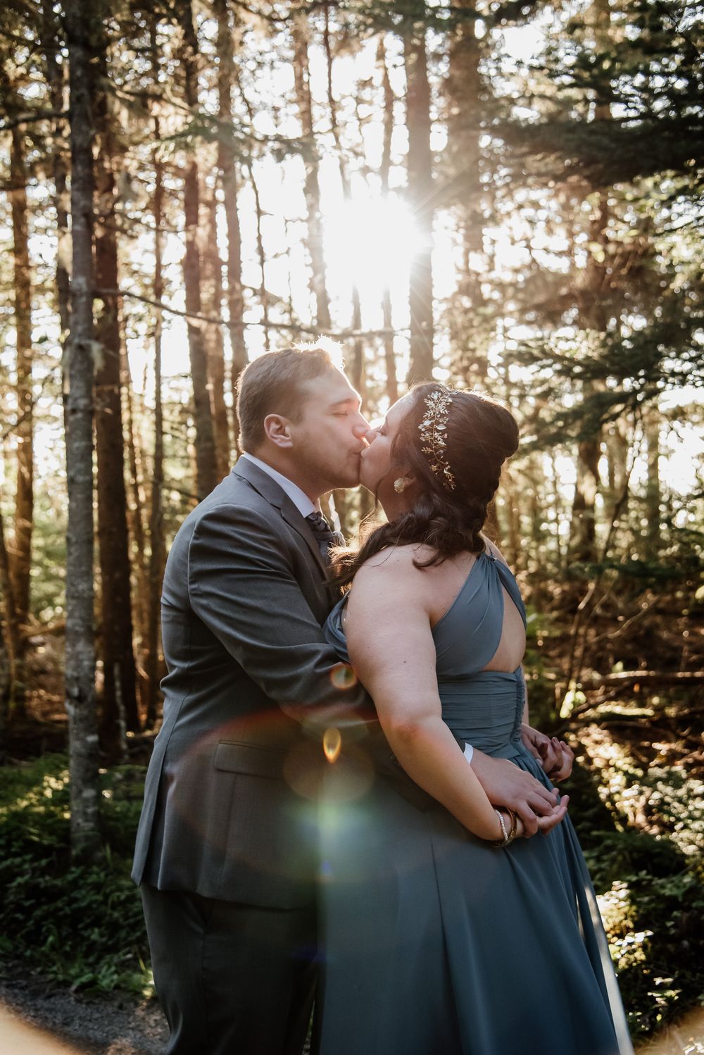 Romantic sunlit forest kiss between couple in formal attire.