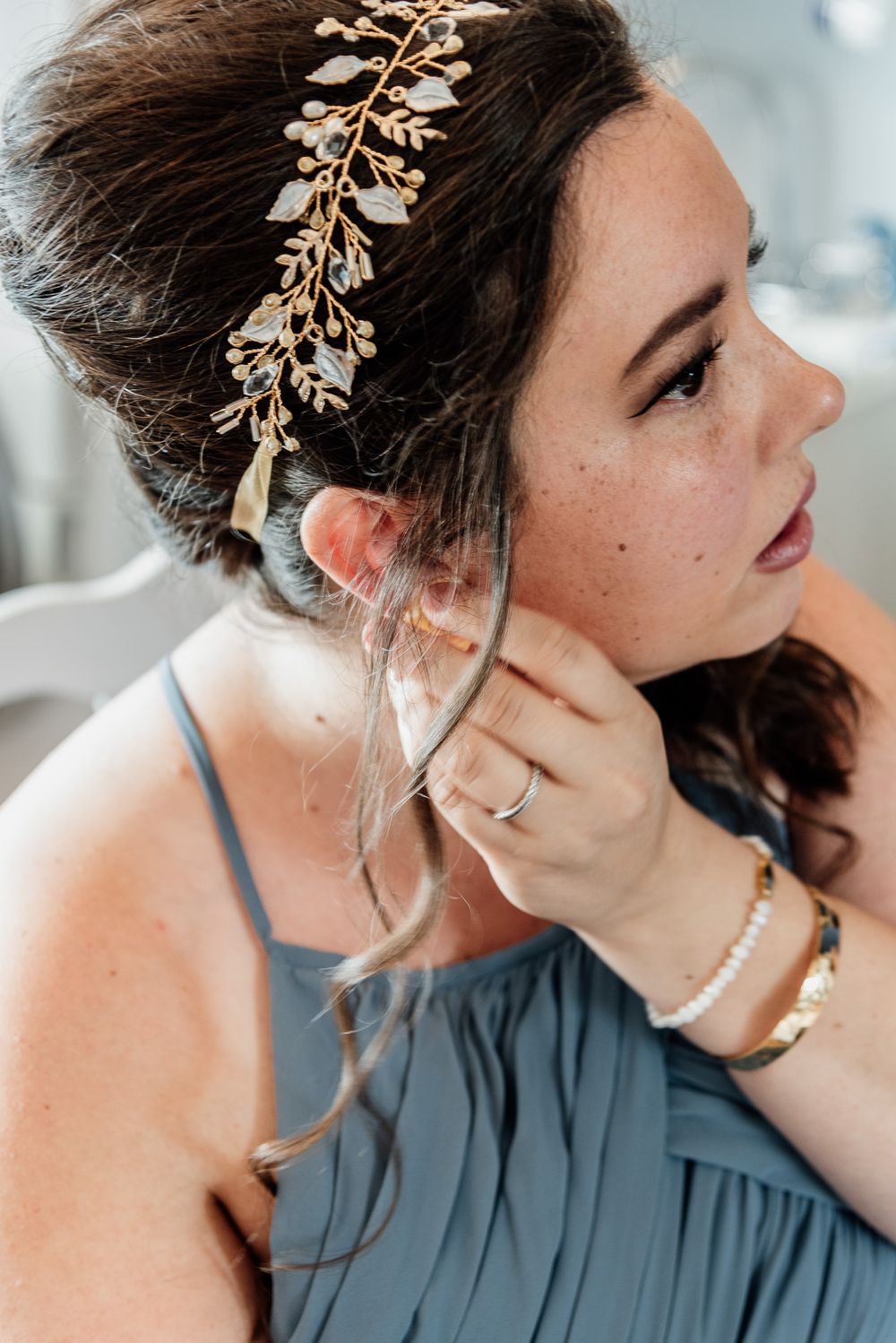 Close-up shot of someone wearing a delicate gold leaf hair accessory and blue dress while getting ready.