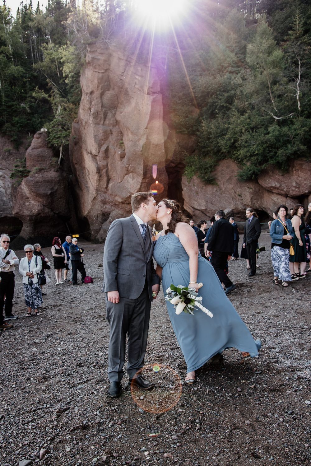 Couple in formal attire sharing a romantic moment in front of dramatic rock formations at sunset.