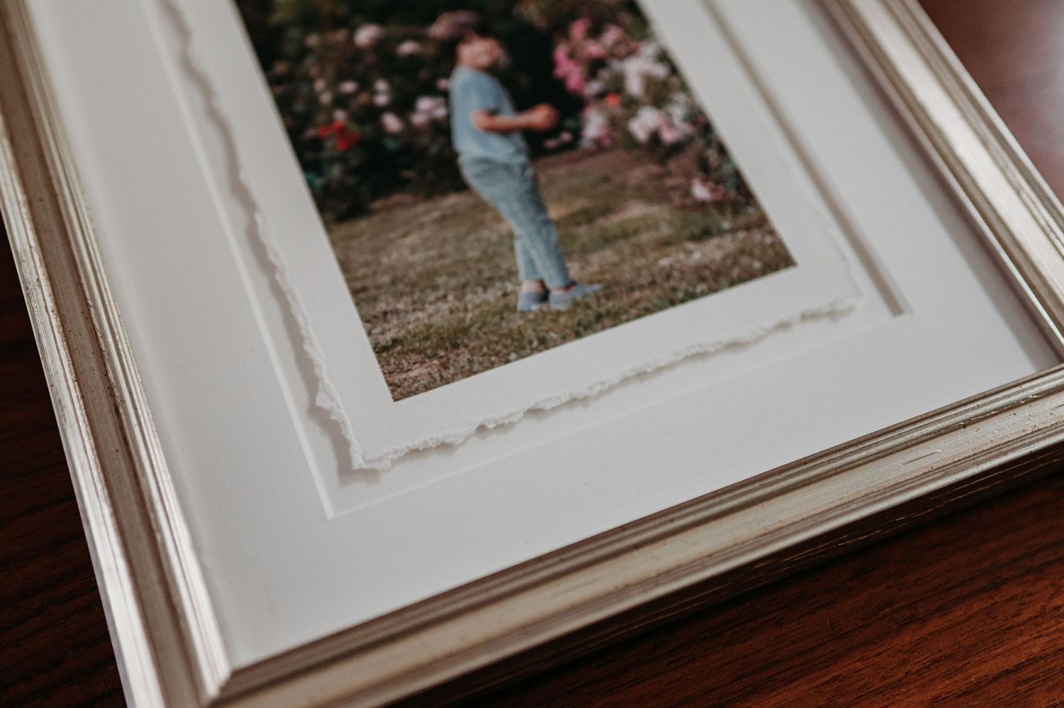 A white matted photograph frame displaying a vintage style image with deckled edges on a dark wooden table.