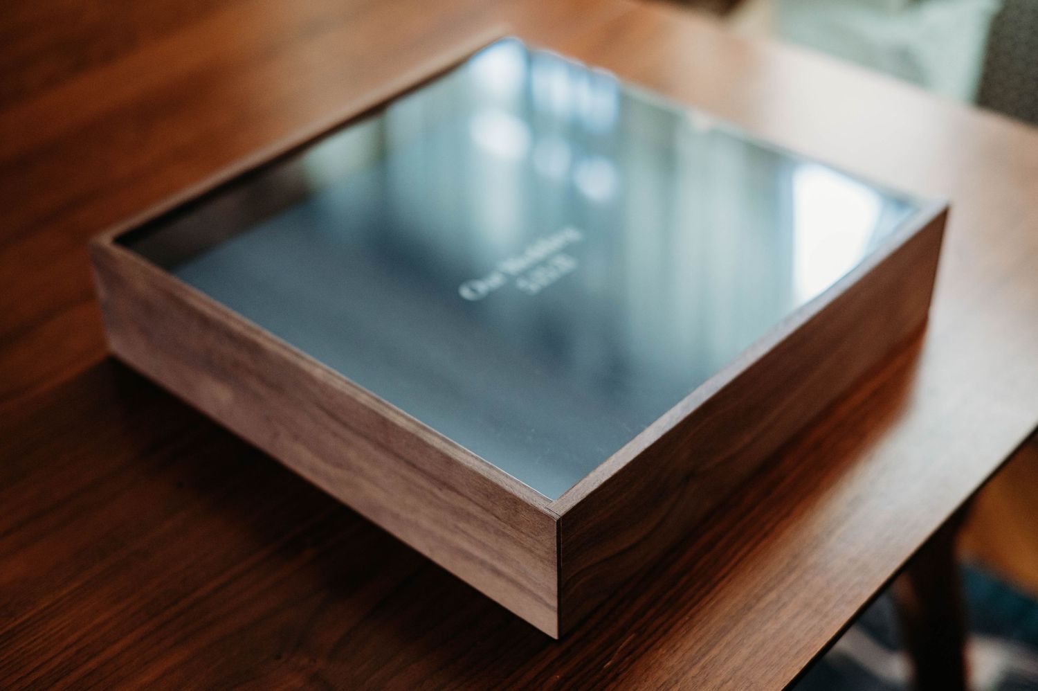 A sleek metal and wood and acrylic box device sits on a wooden surface in soft lighting.