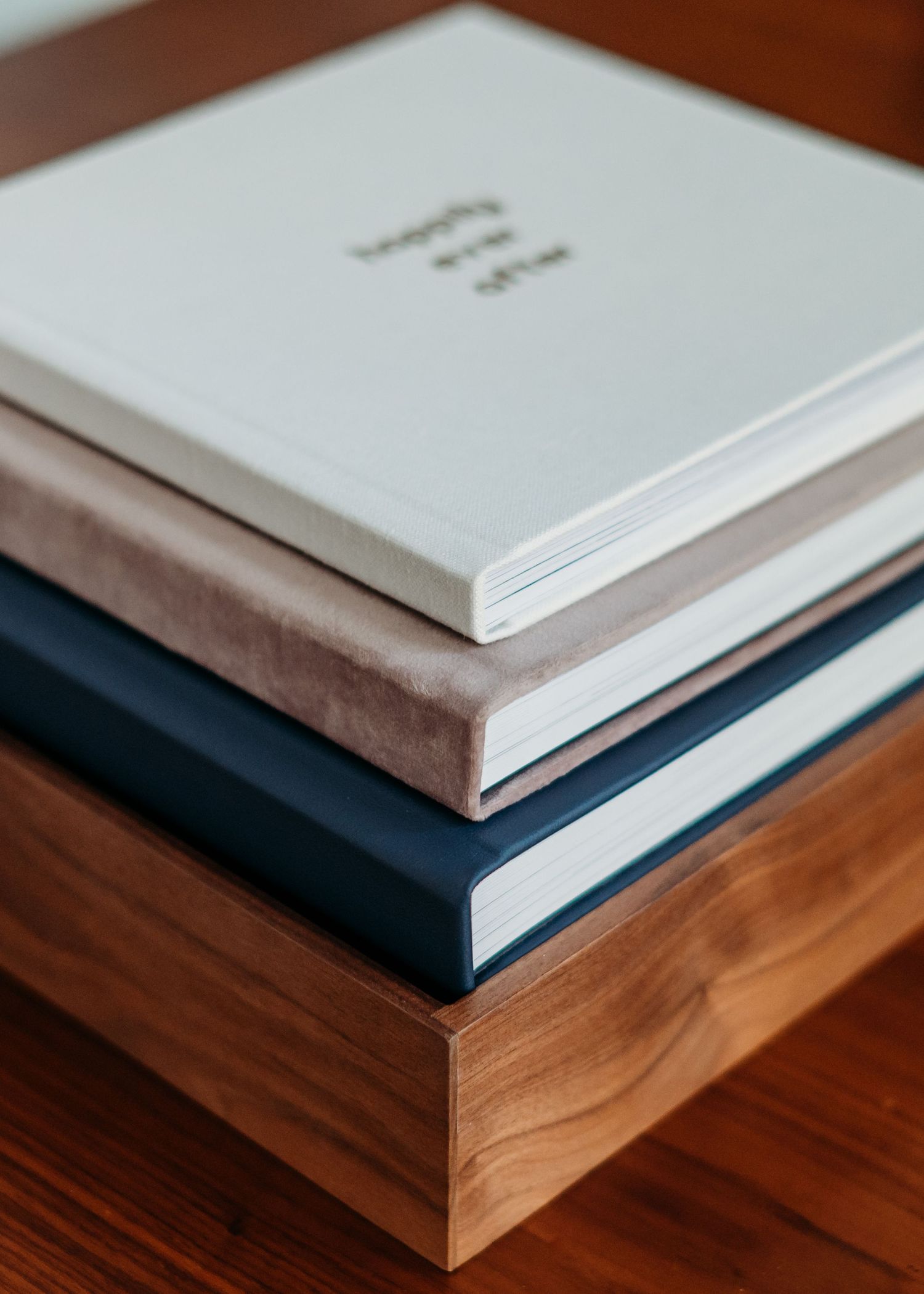 Stack of minimalist books with white, beige and navy covers arranged on a wooden surface.