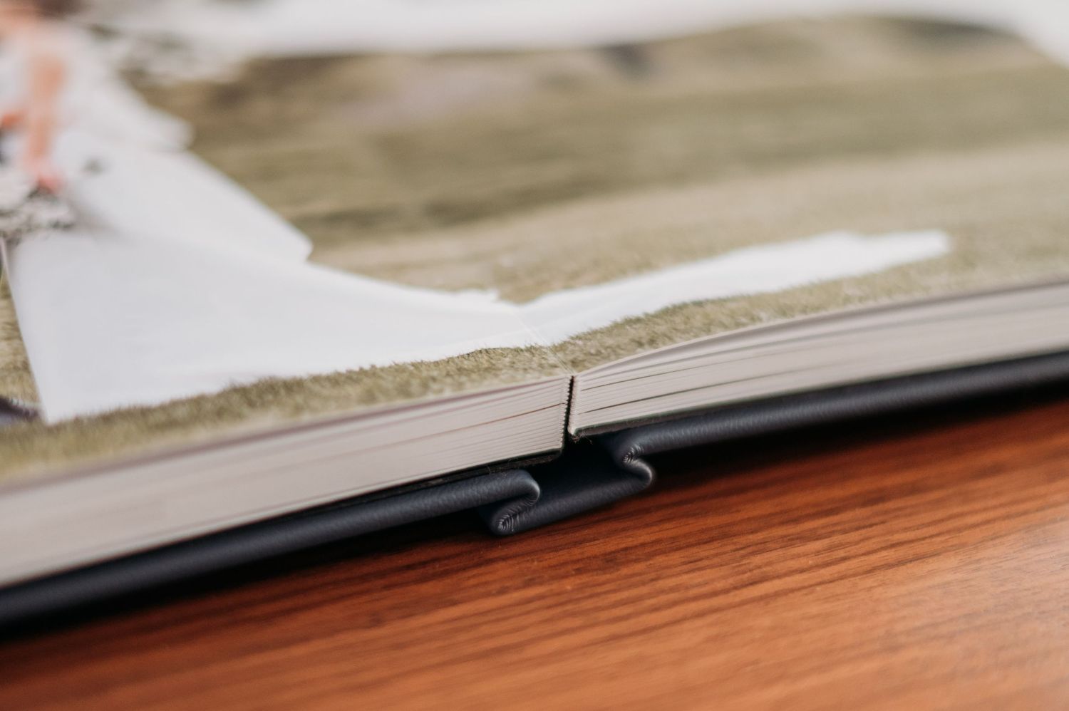 Close-up view of a photo album binding detail on a wooden surface to show thick pages and lay flat binding.