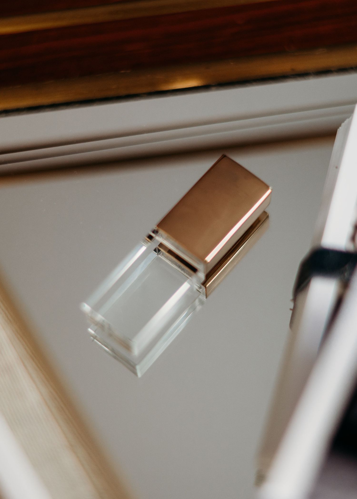 A minimalist crystal glass USB flash drive with a rose gold metallic cap sitting on a mirrored surface.