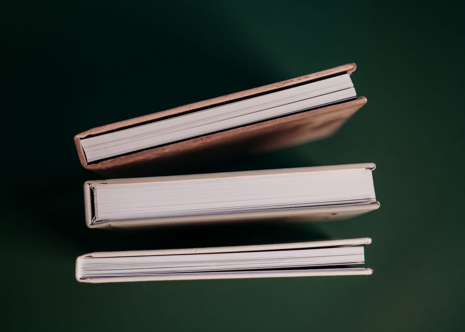 Three hardcover books stacked diagonally against a dark green background.