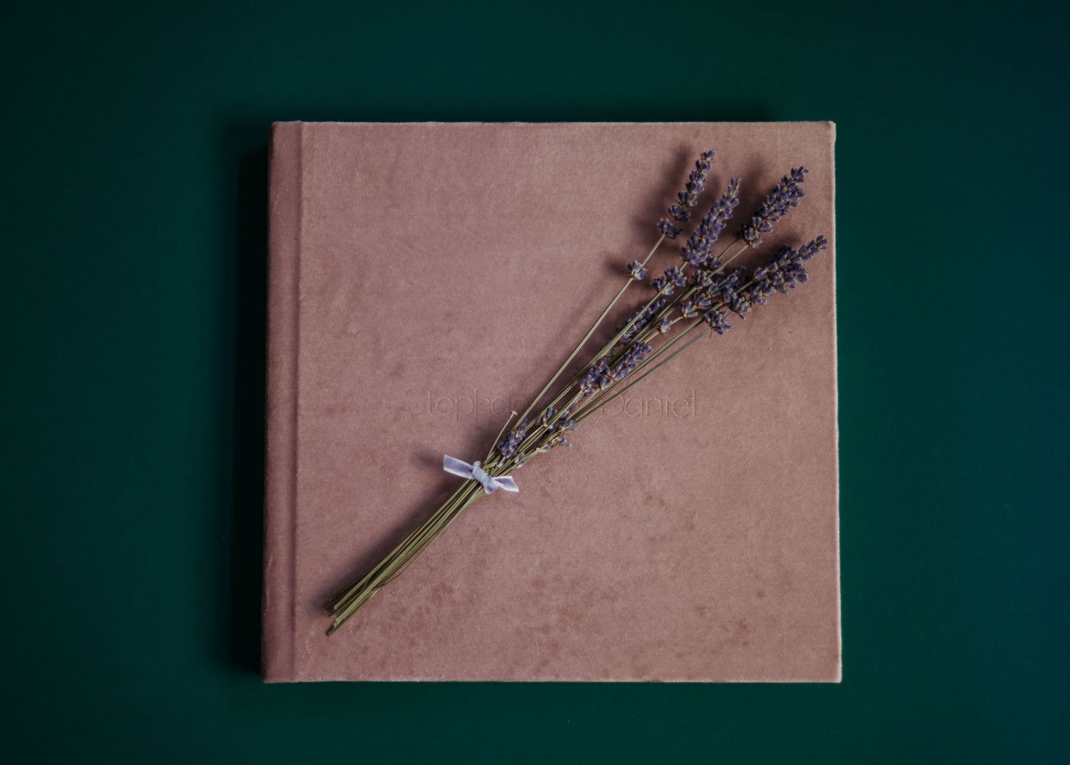 A bundle of dried lavender tied with twine rests on pink paper against a dark green background.