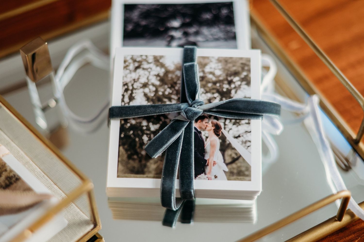 Stack of wedding photographs tied with an elegant navy blue ribbon on a reflective glass surface.
