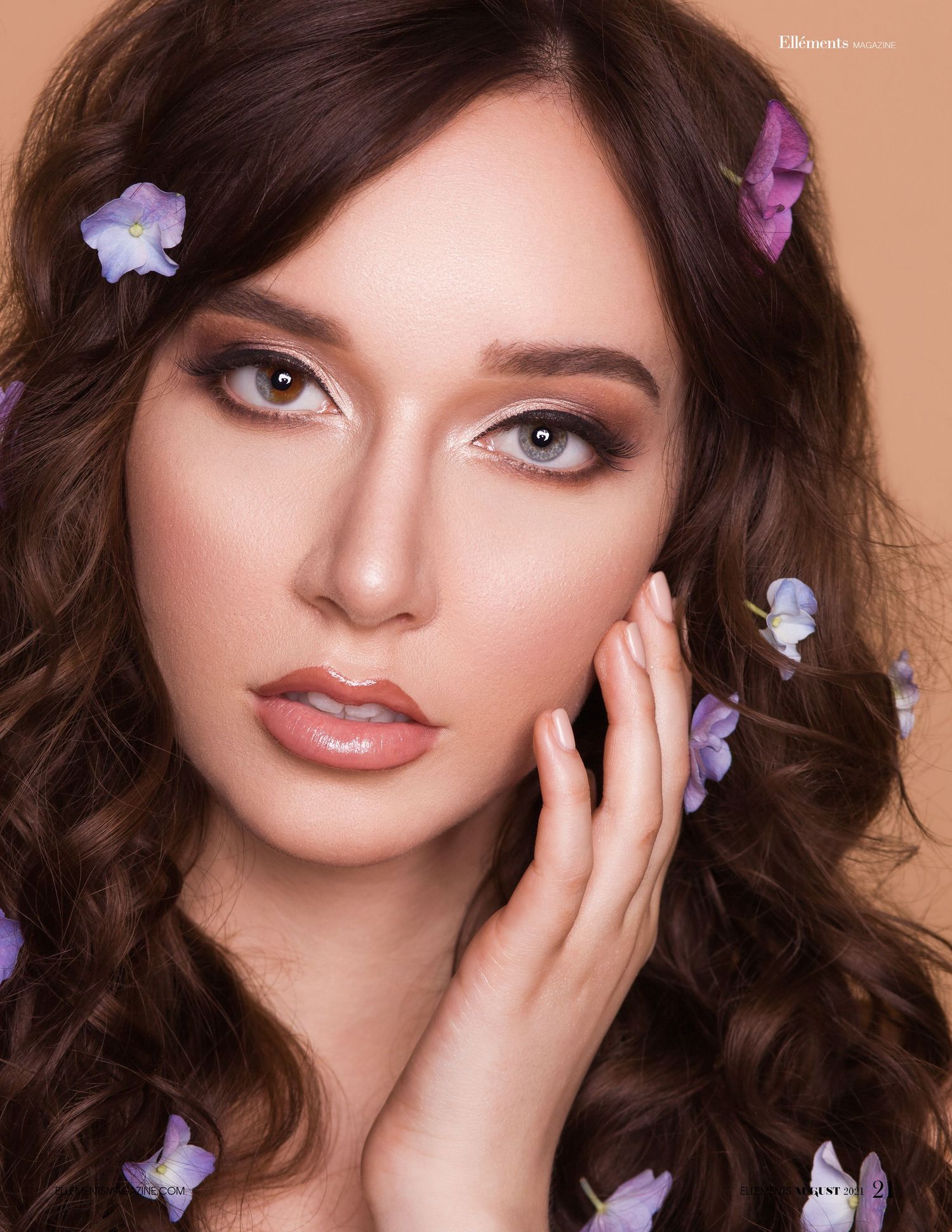 A beauty portrait with wavy brown hair adorned with delicate purple flowers and soft glamorous makeup.