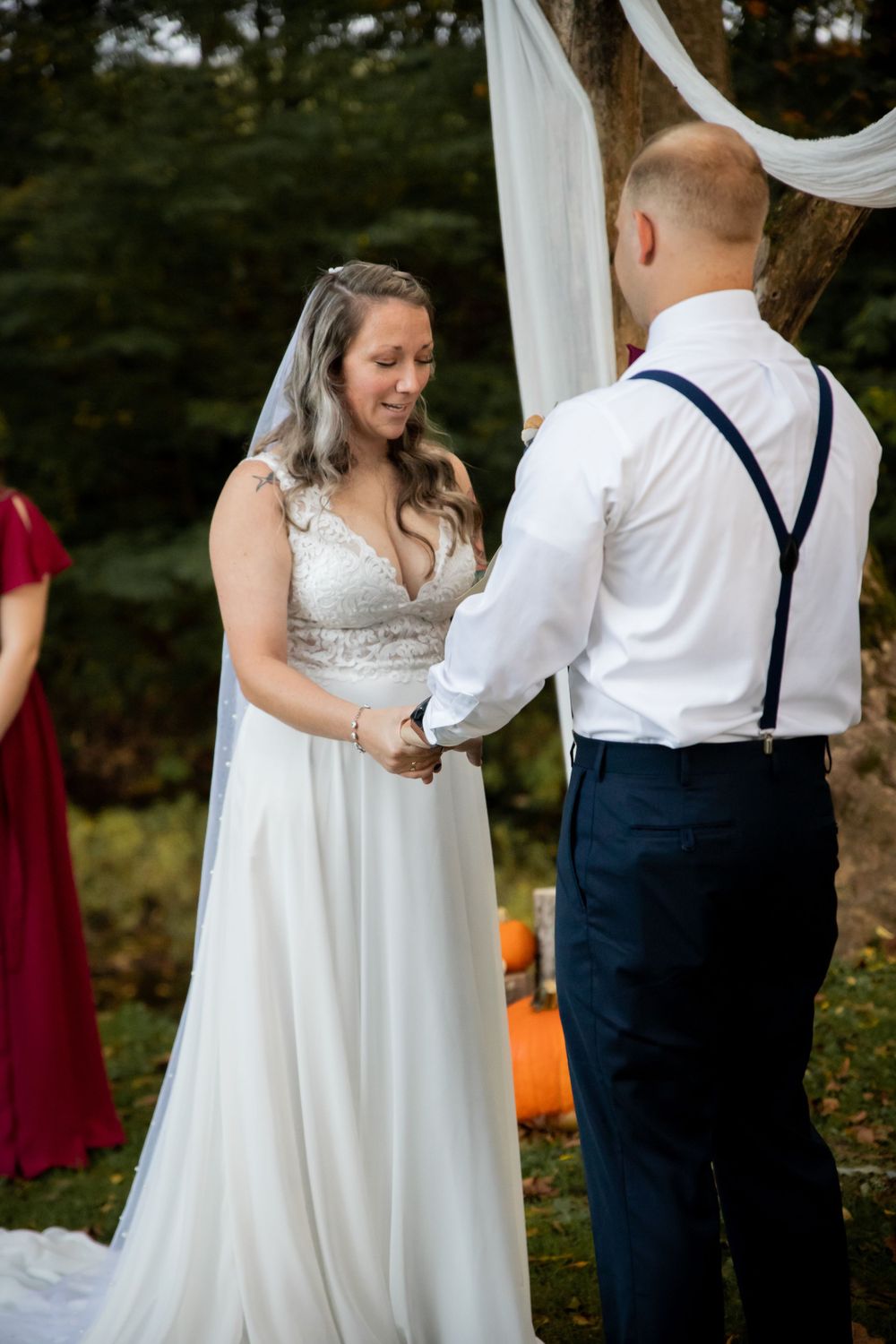 Bride and groom hold hands during outdoor wedding ceremony with autumn decorations.