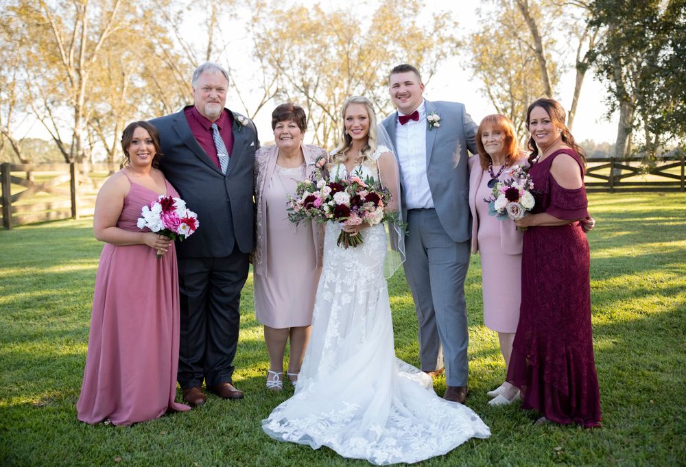 Bride and groom posing with family members including bridesmaids in pink dresses on green lawn at outdoor wedding.