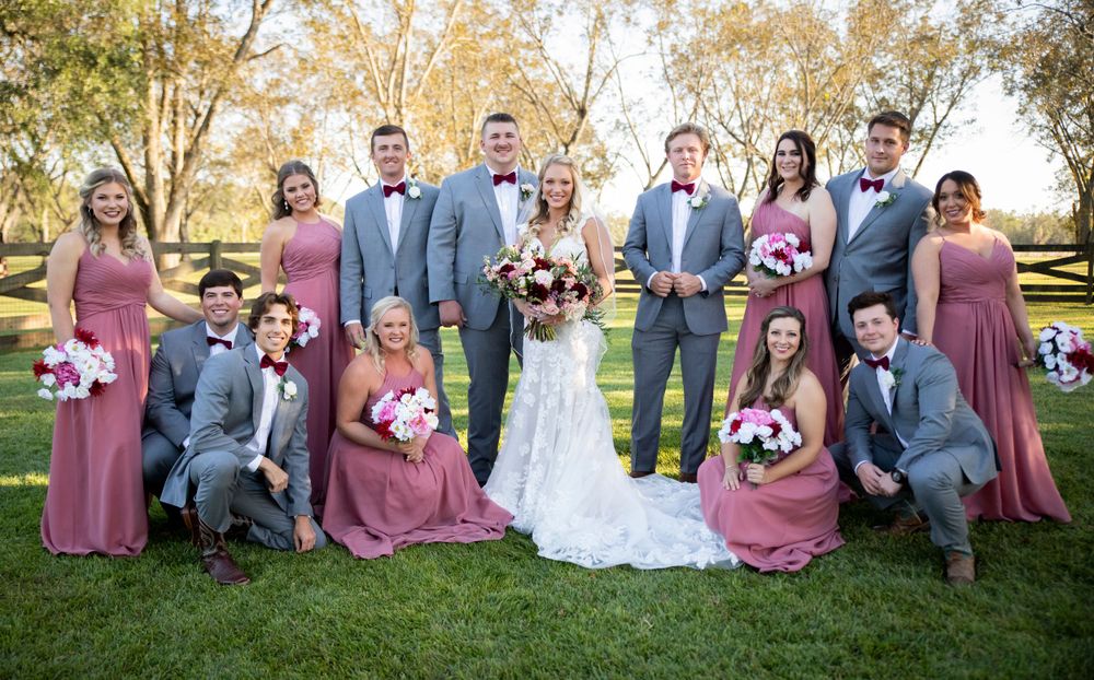 Wedding party posing outdoors with bride and groom, groomsmen in gray suits and bridesmaids in dusty rose gowns.