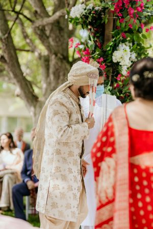 Traditional Indian wedding ceremony with cream and gold attire under floral decorations.