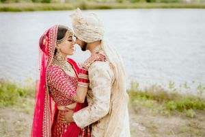 Intimate moment between newlyweds in traditional Indian attire by waterfront.