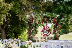 Garden wedding ceremony setup with white chairs under a floral arch with red heart decoration.