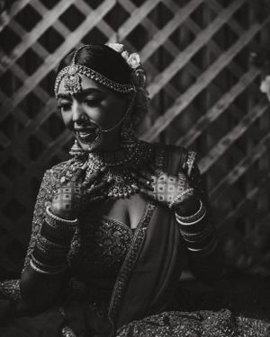 Dramatic black and white portrait of a bride wearing traditional South Asian bridal jewelry and attire.