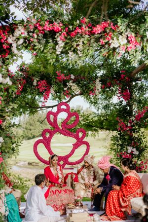 Outdoor wedding ceremony under floral archway with red heart-shaped decorative element.