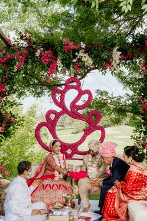Traditional Indian wedding ceremony setup with red and white floral arch and decorative heart backdrop.