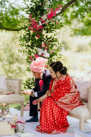 Traditional Indian wedding ceremony takes place outdoors with bright red and pink floral decorations.