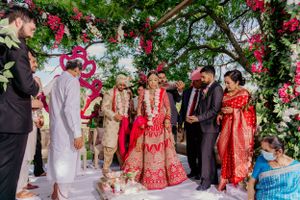 Wedding ceremony group gathered under pink and white floral arch during outdoor celebration.