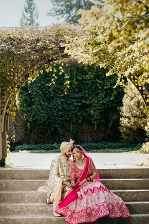 Romantic wedding couple sitting on stone steps under flowering garden arch.