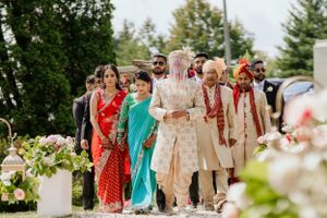 Wedding party walks together in traditional Indian attire through garden path.