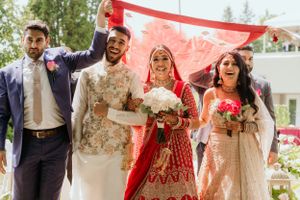 Joyful wedding party celebrates under red canopy during outdoor ceremony.