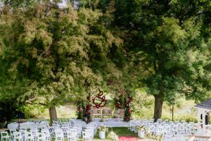 Outdoor wedding venue with white chairs set up under trees and decorated with a heart-shaped arch.