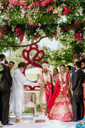 Traditional wedding ceremony under arch decorated with red and white flowers.