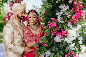 Romantic moment captured under pink and white flower arch during traditional Indian wedding.