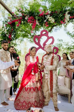 Wedding ceremony under floral arch with red heart design and traditional Indian outfits.