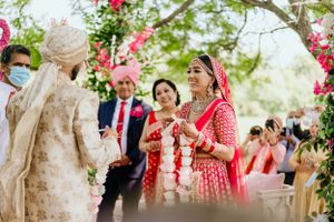 Outdoor Indian wedding ceremony with guests gathering under pink floral decorations.