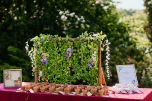 Wedding dessert table decorated with a green plant wall and hanging white flowers.