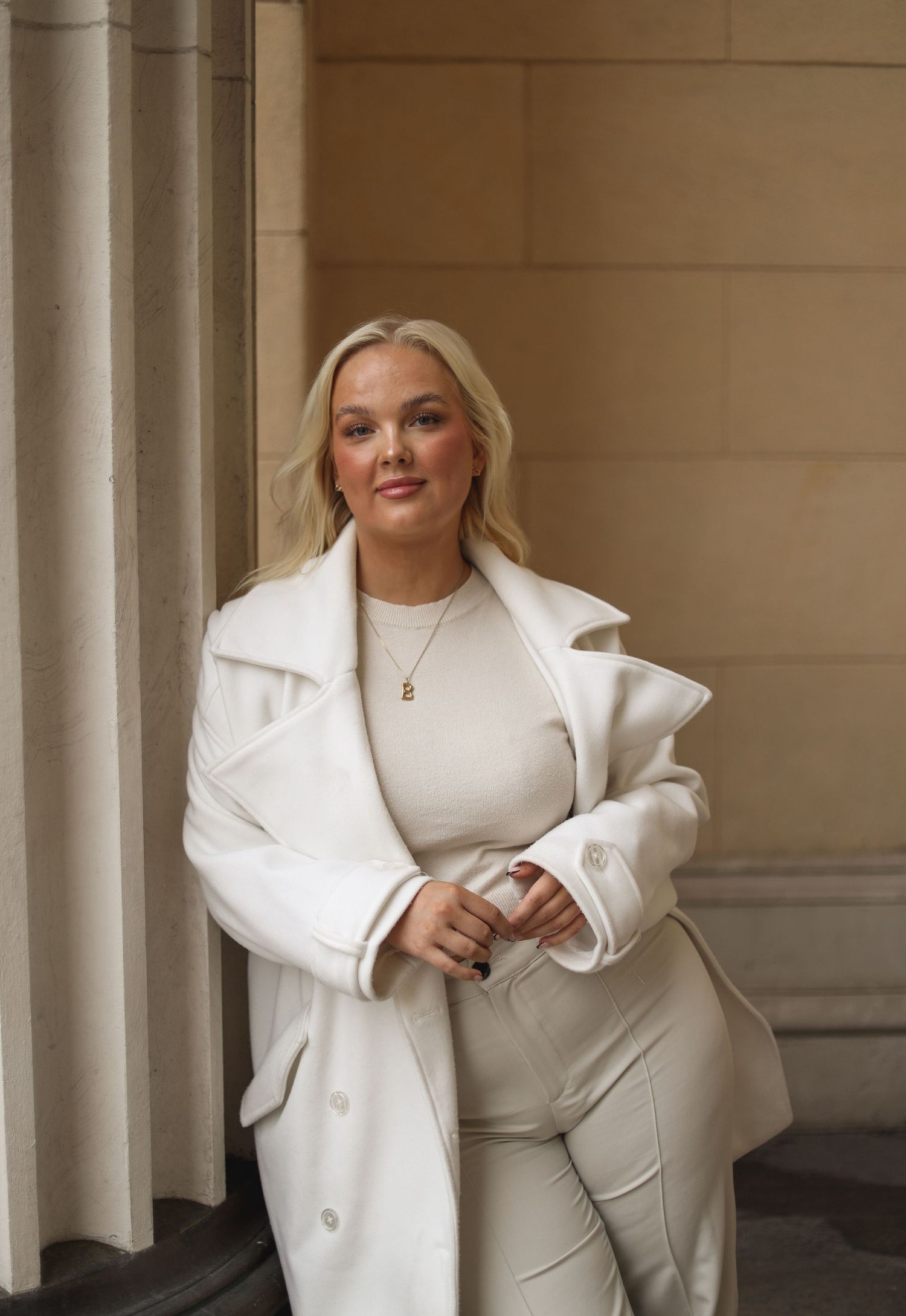 A person wearing an elegant all-white outfit poses confidently against architectural pillars.