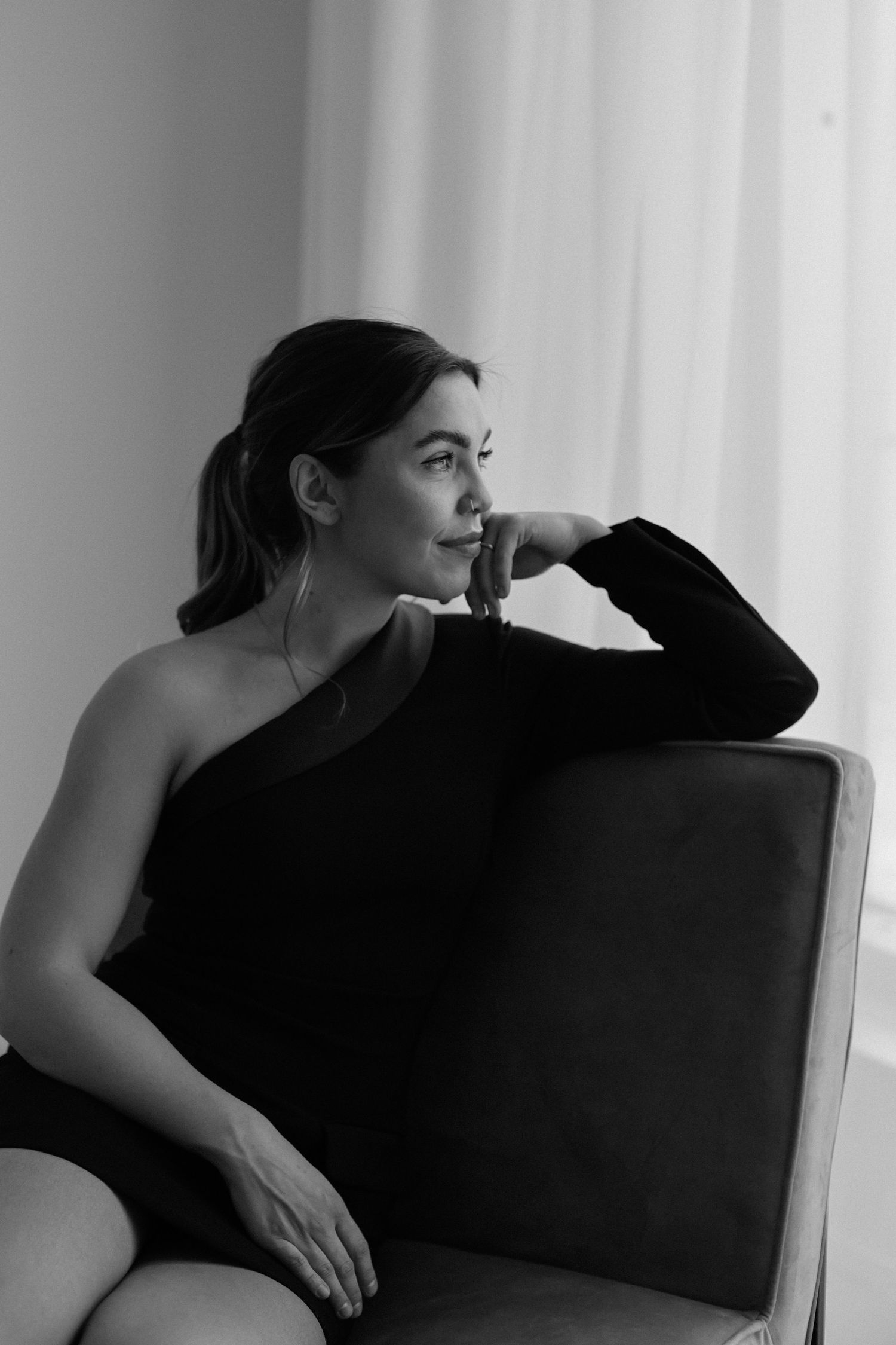 Black and white portrait of woman in one-shoulder top looking pensively to side.