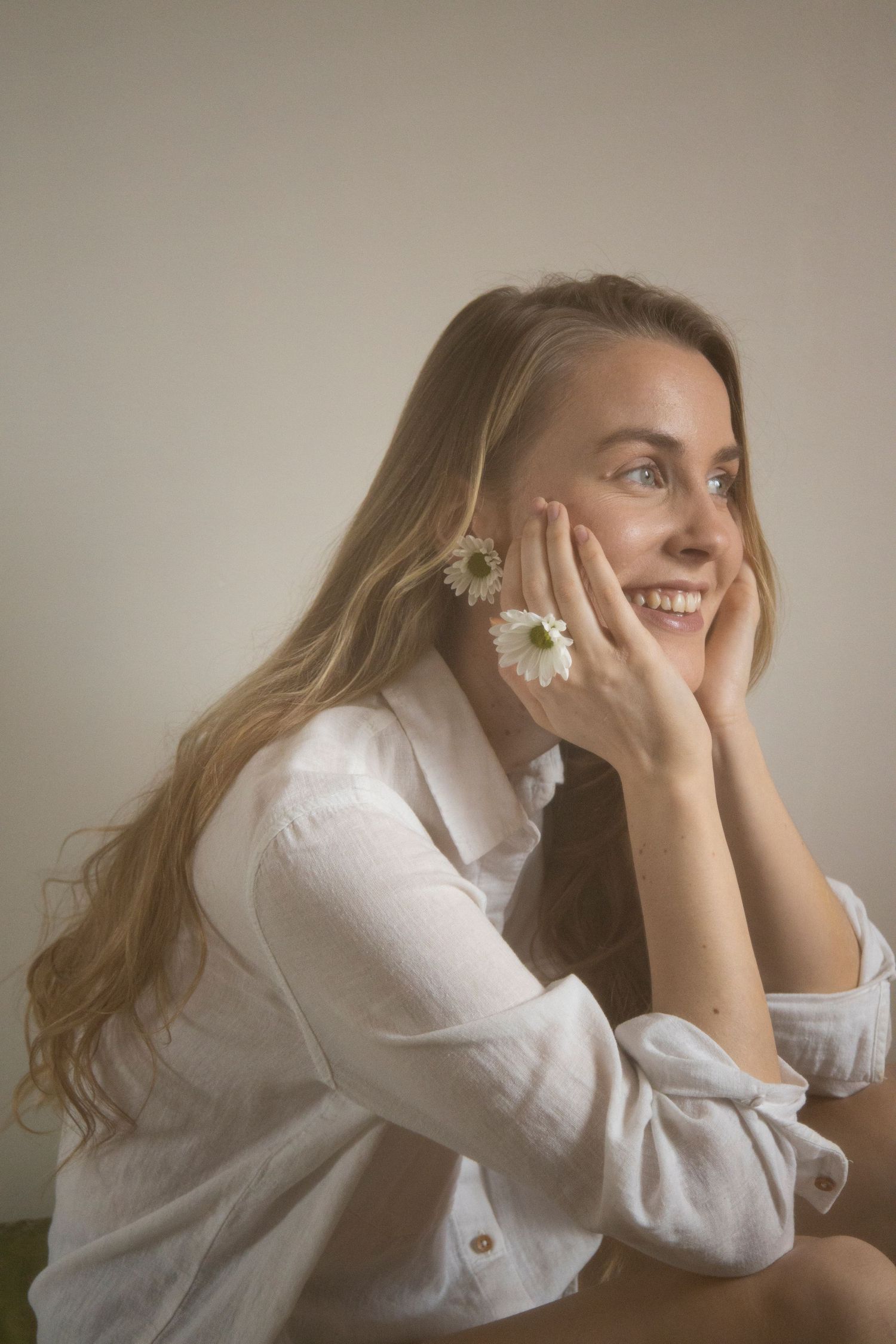 A person in white poses dreamily with small flowers against their face in soft lighting.