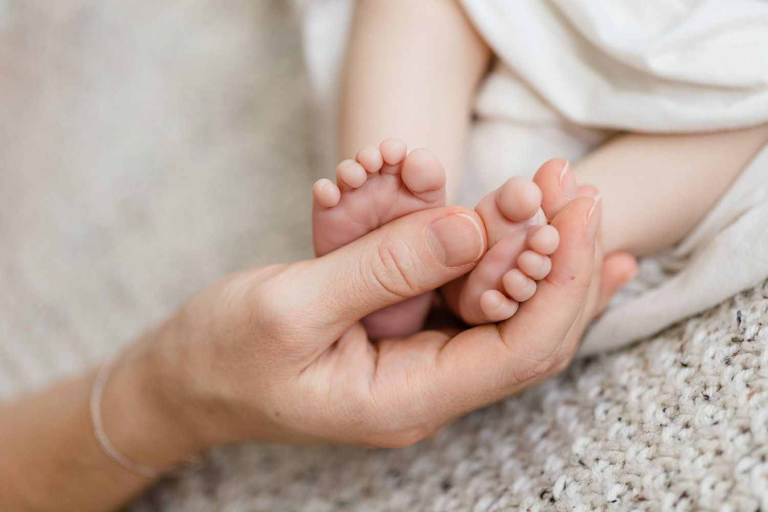 Neugeborenen-Fotoshooting, Detailaufnahme von Babyfüßen in Mamas Händen