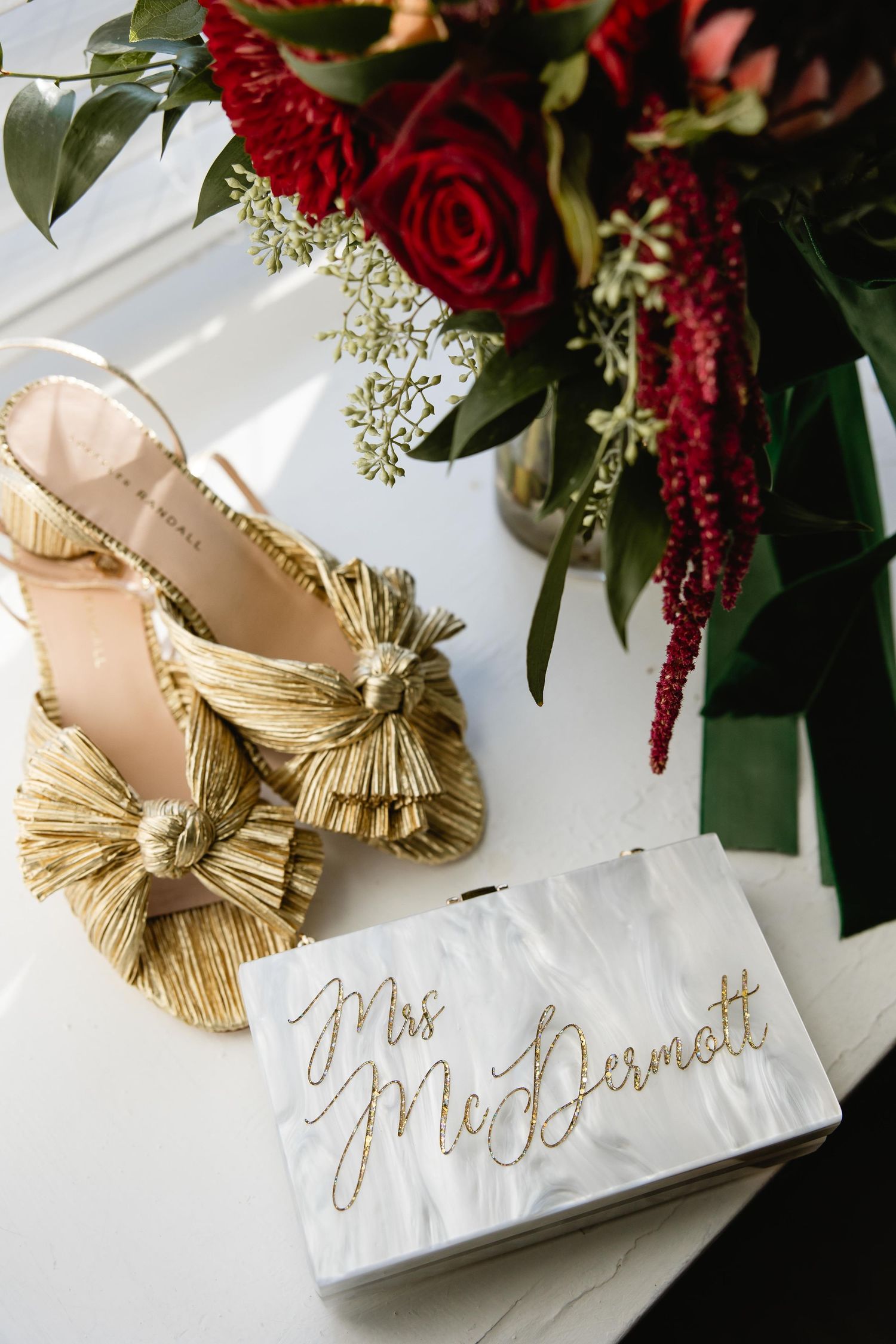 Red roses and floral arrangements next to gold embellished bridal shoes with handwritten name cards.