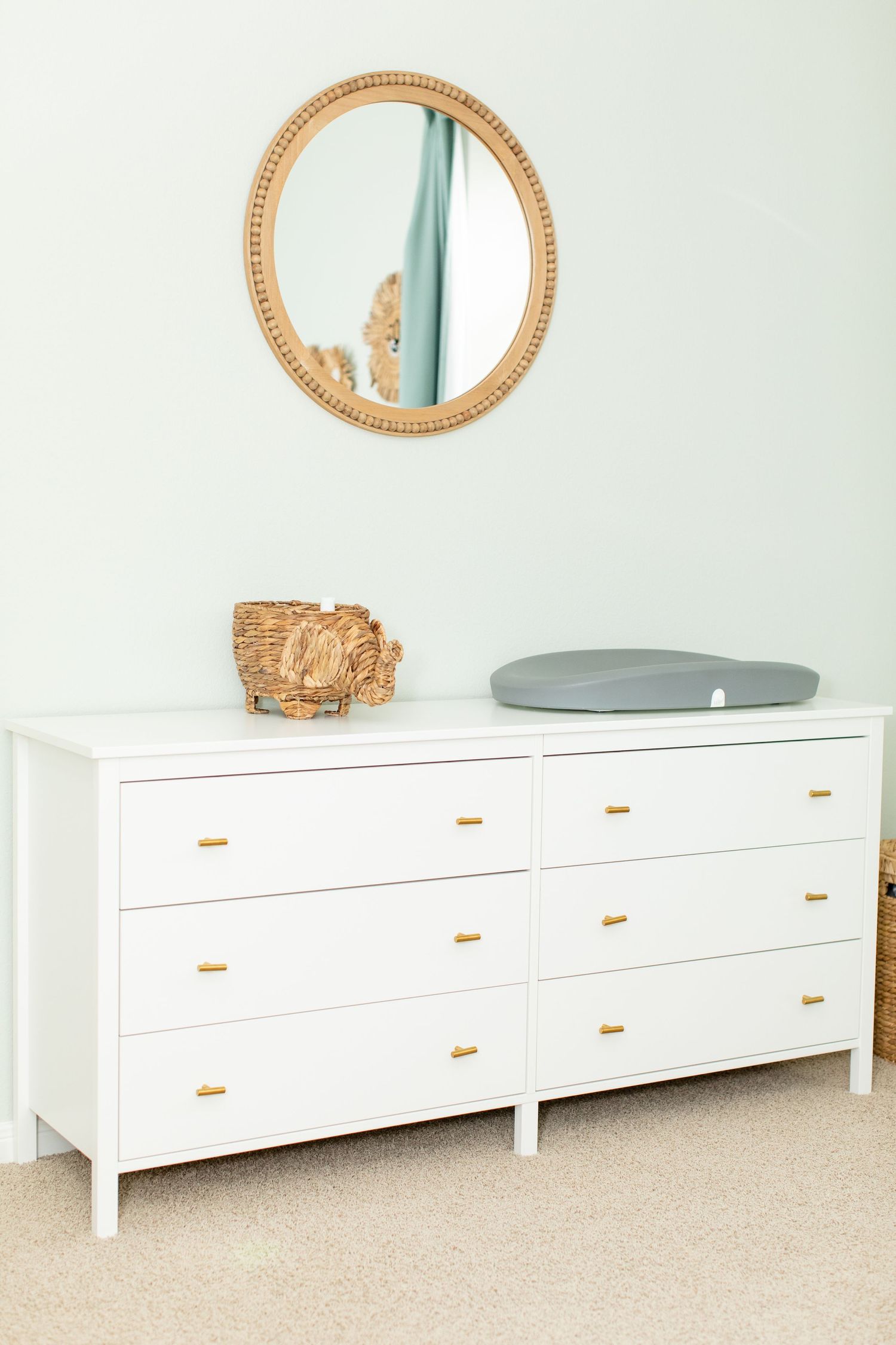 White dresser with gold handles and round mirror in neutral nursery.