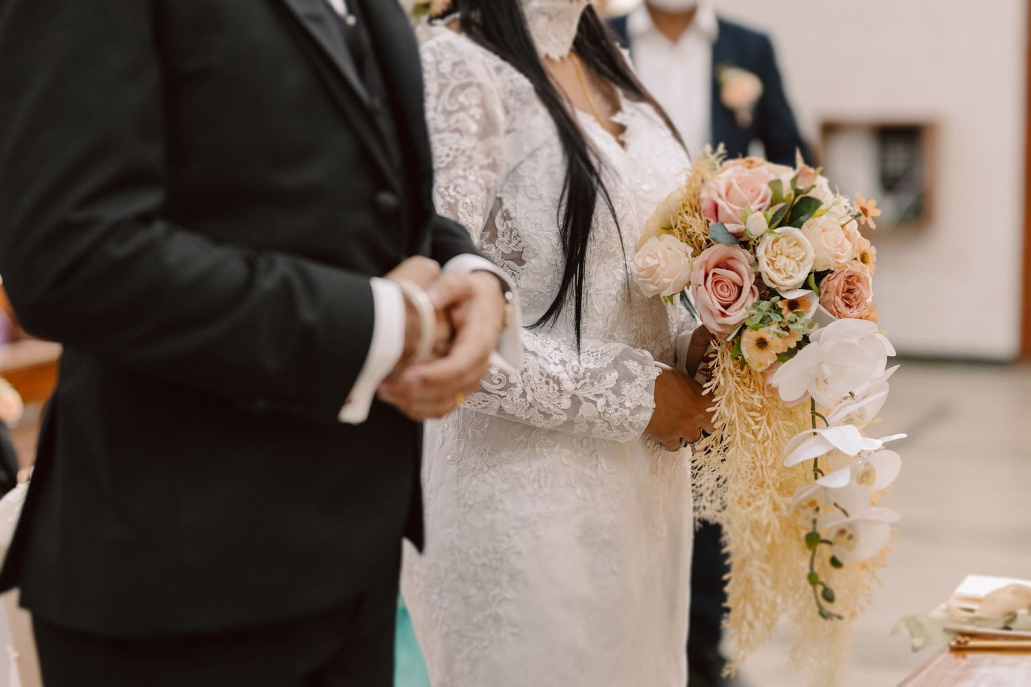 A side view of a bride in lace dress holding a cascading bouquet during the ceremony.